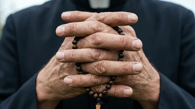 Man priest hands clasped in prayer holding rosary beads, a religious tradition for catholic prayer and faith footage