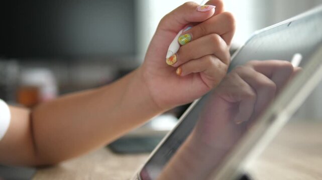 Extreme close-up of a young girl's hand with cute colorful nail art using a white digital stylus to write or draw on a tablet screen, modern e-learning concept