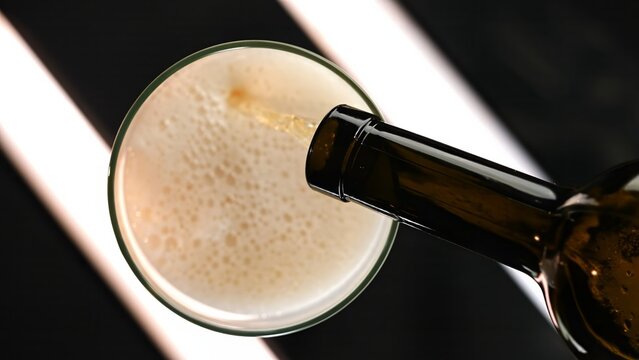 A bottle pouring beer into a glass, creating bubbles, viewed from above. Concept of refreshment, advertising content for bars, pub, cafes, and restaurants, celebration, nightlife and social gatherings