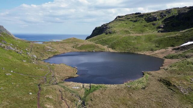 Breathtaking aerial footage moving over the stunning Lake Einangsvatnet, revealing the vast ocean and Kvalvika Beach in the background. Lofoten islands.