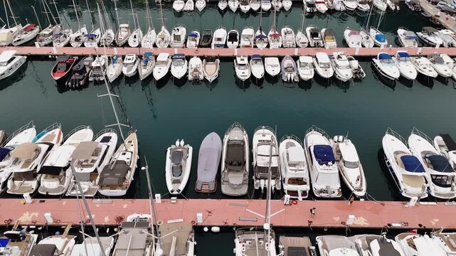 Aerial Marina Shot Showing Boats Docked In Ordered Rows Along Red Piers, Overhead Perspective Captures Calm Turquoise Water, Multiple Yachts And Motorboats Moored, Ropes And Fenders Visible,