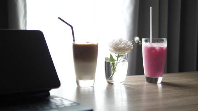 Cinematic close-up of iced latte coffee and Thai pink milk (Nom Yen) in glasses with a white rose in a vase on a wooden table, cafe lifestyle and refreshment concept