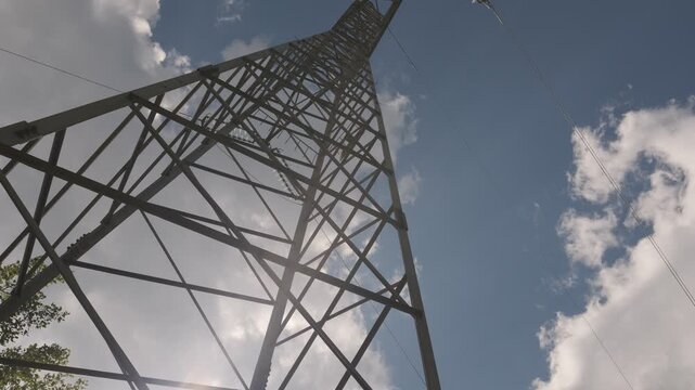 Low angle shot of a high voltage electricity transmission tower against a blue sky with clouds