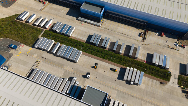Aerial view of Magna Park logistics hub with rows of parked semi-trailers and large warehouse buildings under bright sunlight in Magna Park, England, United Kingdom.