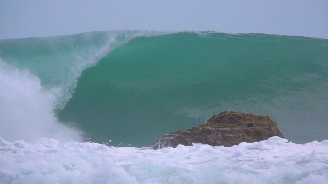 SLOW MOTION: Hollow and powerful turquoise wave breaks over a reef beside a rock as whitewater surges across the foreground. Clean and firing wave conditions in the remote Mentawai Islands, Indonesia.