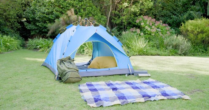 Blue dome tent sitting on grassy lawn, showing yellow bedding, backpack leaning, checkered blanket