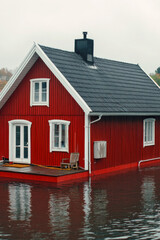 Fototapeta premium A small red house floating on calm waters of a lake, surrounded by greenery vertical frame