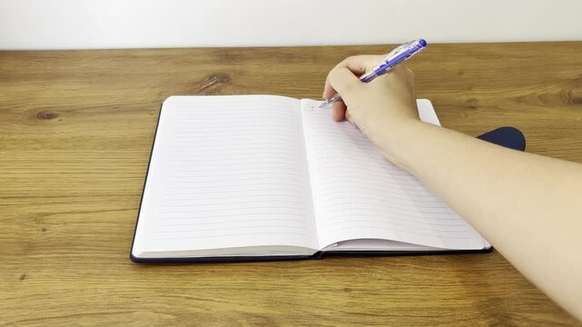 Horizontal close-up video of a person writing in a notebook.