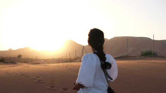 Solo female traveler watching sunset in Dubai desert with golden dunes
