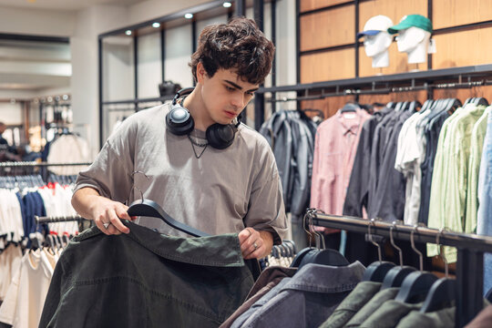 Teen boy shopping for light jacket in clothing store. Young man selecting outerwear. modern style and consumer behavior.