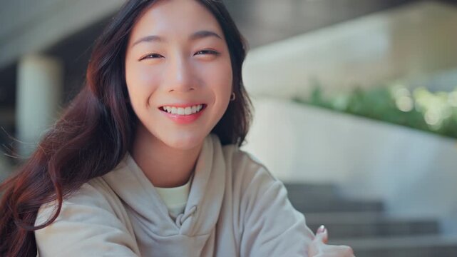 Cheerful young Asian woman smiling at the camera in a modern urban park. Authentic Gen Z lifestyle and happiness concept for education, wellness