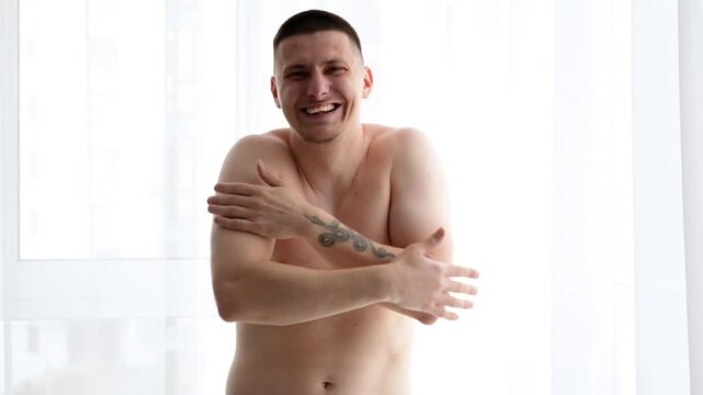 Young muscular man feeling awkward and covering himself with his arms while holding personal items, requesting privacy in a room