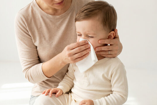 Mother comforting young child while wiping nose in bright room  