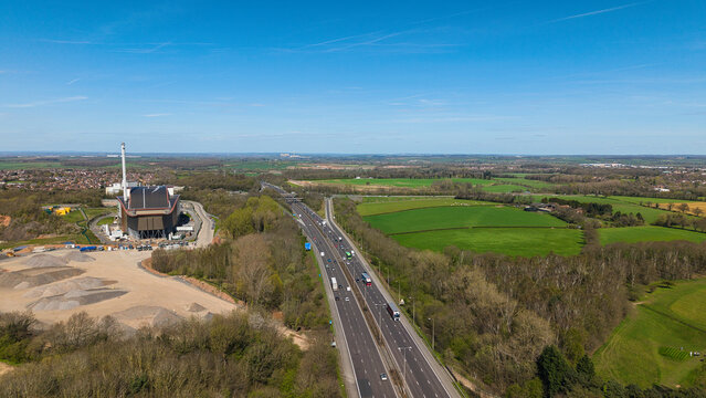 Aerial view of the Encyclis Newhurst ERF facility next to the M1 motorway with traffic flowing past green fields and woodland in Shepshed, England, United Kingdom.