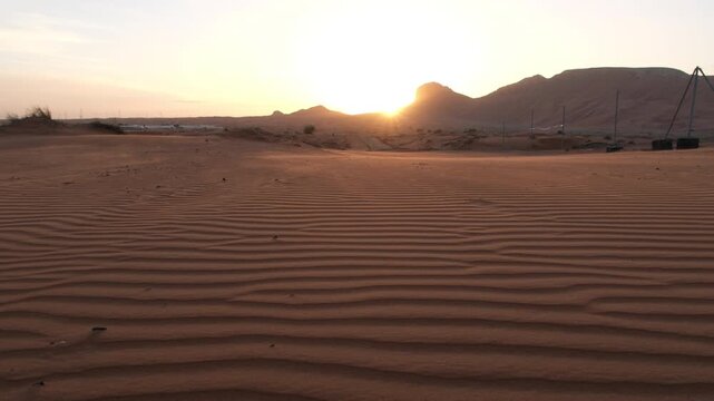 Scenic morning sun rising over textured desert sand patterns and distant rocky mountains in the United Arab Emirates