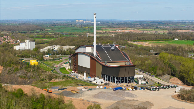 Aerial view of the Encyclis Newhurst ERF industrial facility with its curved roof and tall chimney stack surrounded by green fields and trees in Shepshed, England, United Kingdom.