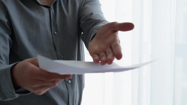 Office worker standing in a bright office while holding printed documents and reading assigned tasks, reviewing work instructions and information.