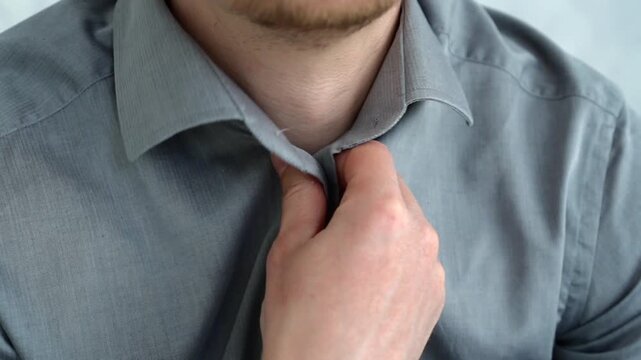 Close-up shot of male hands fastening buttons on a gray shirt, showing business style and workplace dress code preparation.
