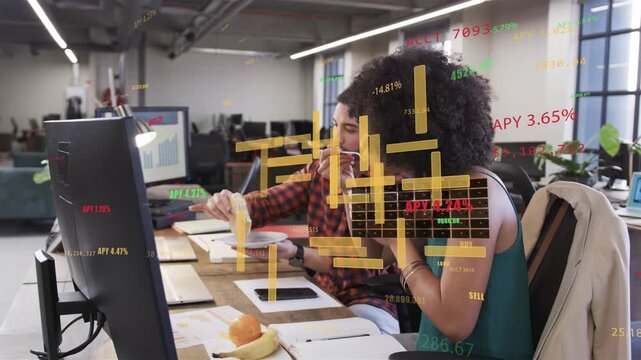 Male coworker pointing at monitor, female colleague leaning in, analyzing animated finance charts