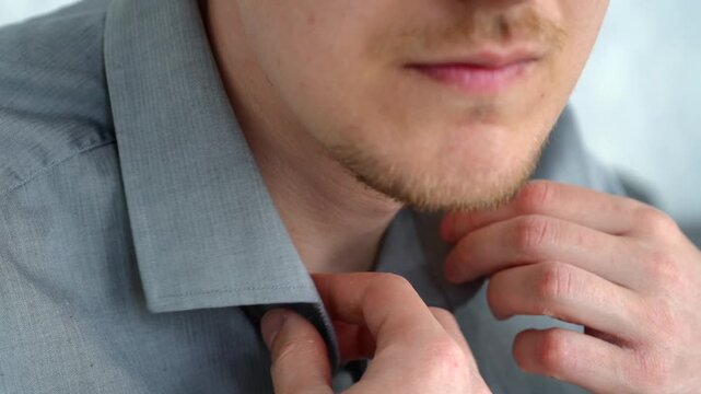 Man dressing in a gray formal shirt, carefully buttoning it as part of his daily office routine and professional preparation.