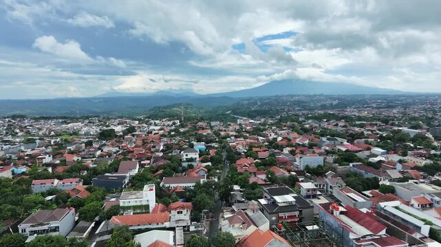 Aerial view of a densely populated city with a majestic mountain background under a cloudy sky.