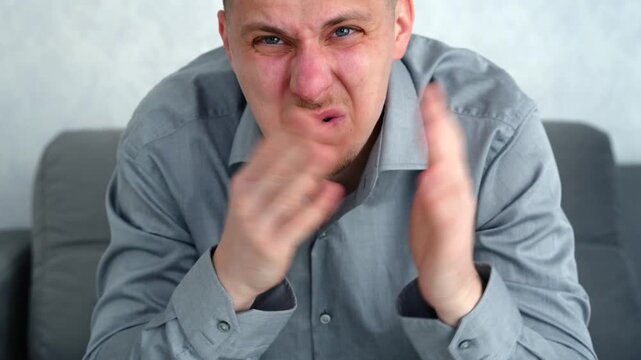 Young man sitting in a light room with a worried expression, covering his nose due to unpleasant air conditions or suspected gas issue.