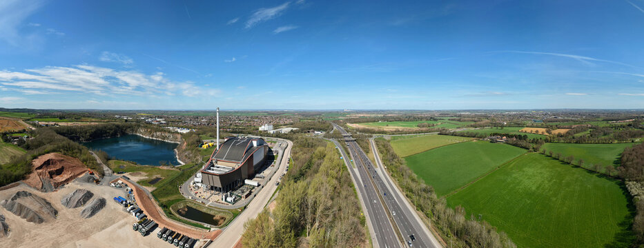 Aerial view of the Encyclis Newhurst ERF facility, adjacent quarry, and the M1 motorway in a wide panorama under a clear blue sky in Shepshed, England, United Kingdom.