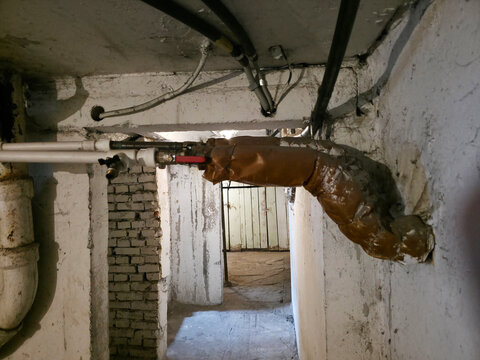 Old pipe with insulation in basement. Utility system repair and maintenance. Plumbing structure in storage area. Industrial infrastructure detail in residential building construction.
