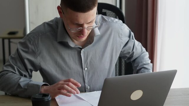 Professional man in office environment studying documents on a desk, concentrating on paperwork and business information processing