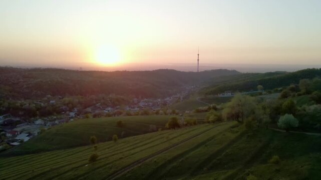 Aerial sunset view of Almaty foothills and Kok Tobe TV tower. Blooming trees in spring, golden hour mountains and city panorama in Kazakhstan. Cinematic drone footage.