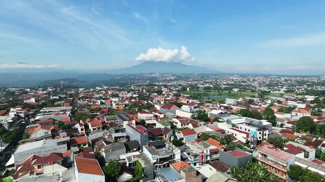 Aerial view of a dense city with a majestic mountain in the background under a blue sky.