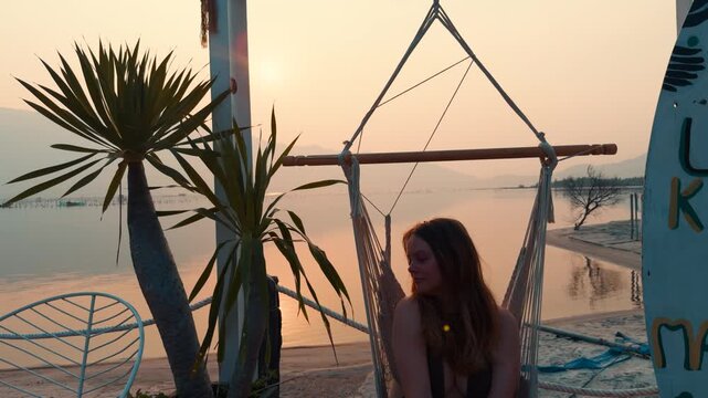 Young woman relaxing in a hammock on the sandy beach during sunset, enjoying a tranquil tropical vacation with warm light reflecting on the calm water