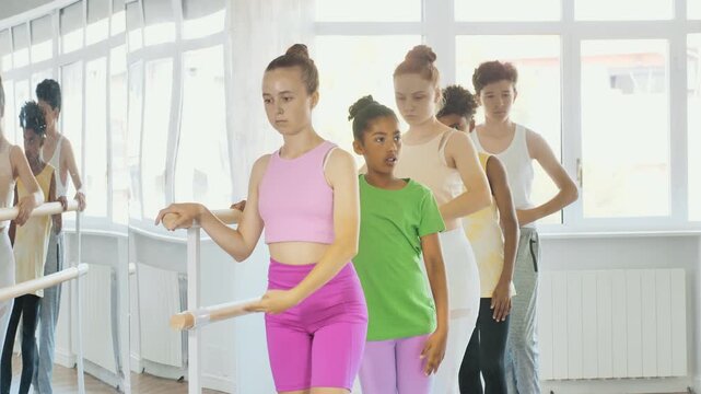 Slim teenage attendees of ballet courses training battement tendu position under control of ballet-master in dance studio. High quality 4k footage