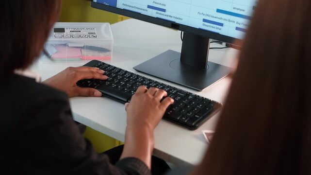 Professional employee typing on a computer keyboard in a modern office. Over the shoulder view of worker managing project tasks and data analysis on a monitor for business productivity at desk