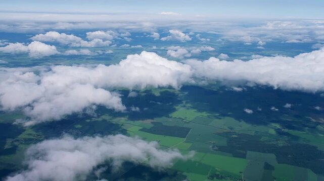 Aerial view from airplane of green meadows. White cumulus clouds in blue sky. Travel, freedom concept. Aviation, transportation