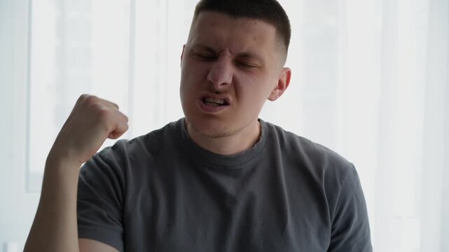Young man mimicking self punches in front of camera, exaggerating reactions as if rehearsing a fight scene. Indoor bright environment.