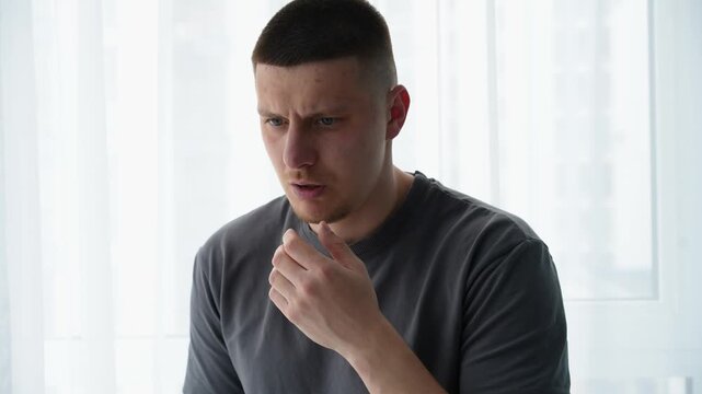 Close-up of a man in a gray t-shirt dealing with hiccups, showing a brief discomfort and involuntary reaction.