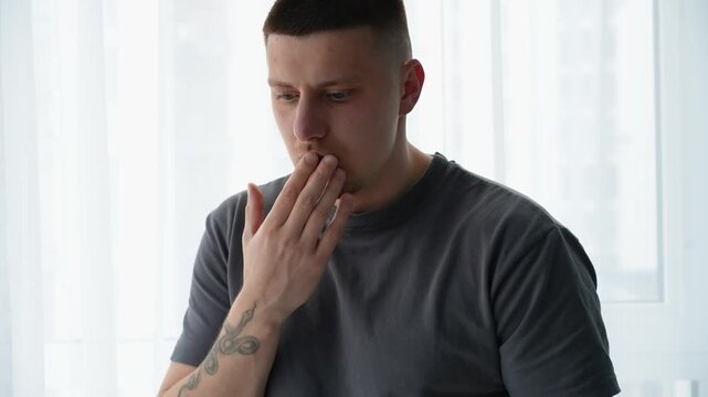 Man with short hair experiencing hiccups indoors, showing mild discomfort and surprise, possibly after eating or drinking fast.