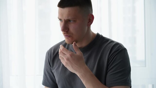 Young man suddenly hiccuping and reacting with confusion in a bright room. Everyday situation after a quick meal or drink.