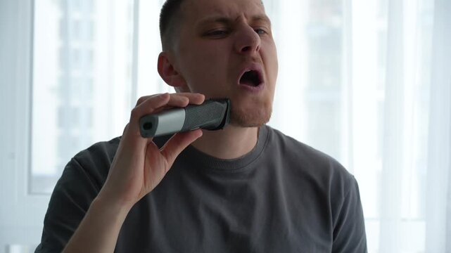 Man using an electric trimmer to adjust beard and mustache length at home, preparing his appearance before a meeting or date. Close-up grooming routine.