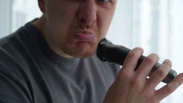 Man using an electric trimmer to adjust beard and mustache length at home, preparing his appearance before a meeting or date. Close-up grooming routine.