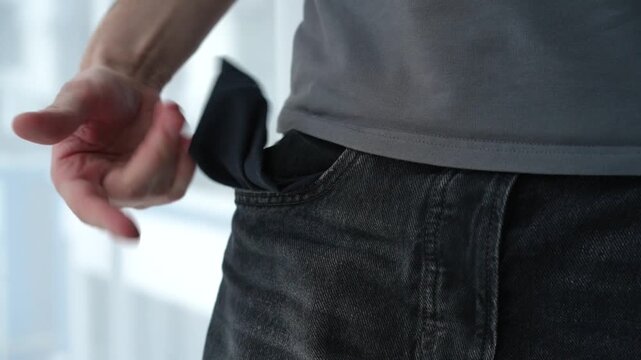Young man showing empty pockets of his black pants, indicating that he has no money. Concept of financial difficulty and lack of funds