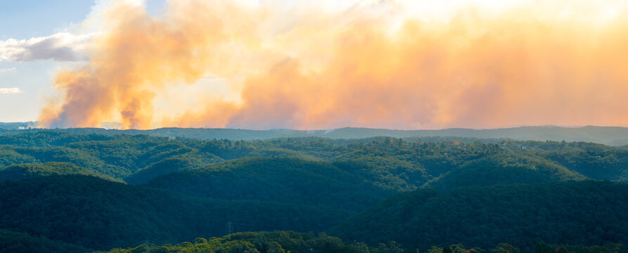 Thick orange smoke across the ridgeline caused by hazard reduction burning in the late afternoon as the sun was setting in the Blue Mountains in New South Wales, Australia