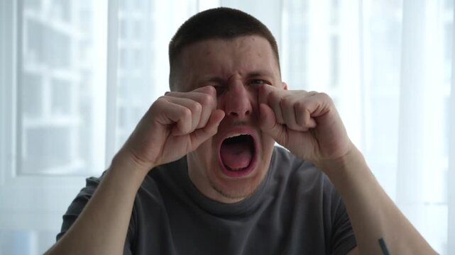 Young man gesturing like he is crying and complaining, with playful facial expression and exaggerated emotional reaction in an indoor bright setting.