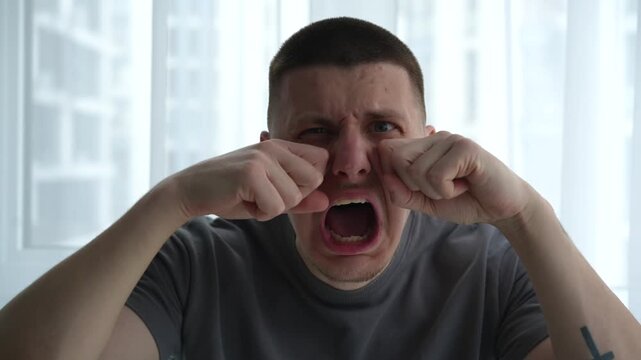 Close-up of a young male using his hands to mimic wiping tears from his face, making a humorous and exaggerated sad expression. Concept of playful behavior and irony