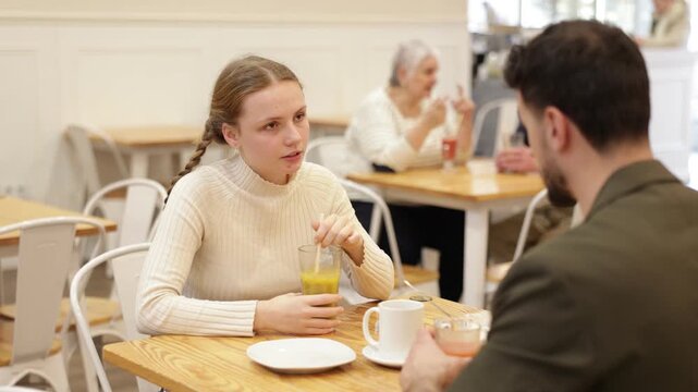 Father and teenage daughter sitting at table in cafe. Light snack or coffee break at restaurant, family getaway or pastime. Family time, Sunday lunch at chain cafe in capitals pedestrian tourist area