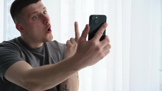 Young man during a smartphone video call making an offensive hand gesture toward the screen, expressing anger and conflict in online communication. 