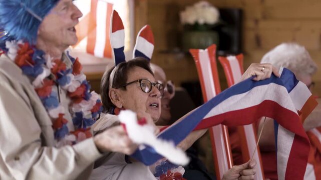 Happy senior soccer fans cheering for france and austria from at home watching football match
