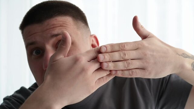 Young man in a bright room playfully covering and uncovering his face with his hands, rapidly changing facial expressions and mood. Concept of shifting emotions and playful behavior.