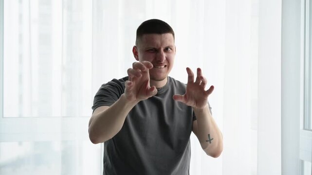 Young brunette man in a bright room making playful hand gestures as if flirting or jokingly trying to attract someone&rsquo;s attention. Concept of lighthearted interaction and social confidence